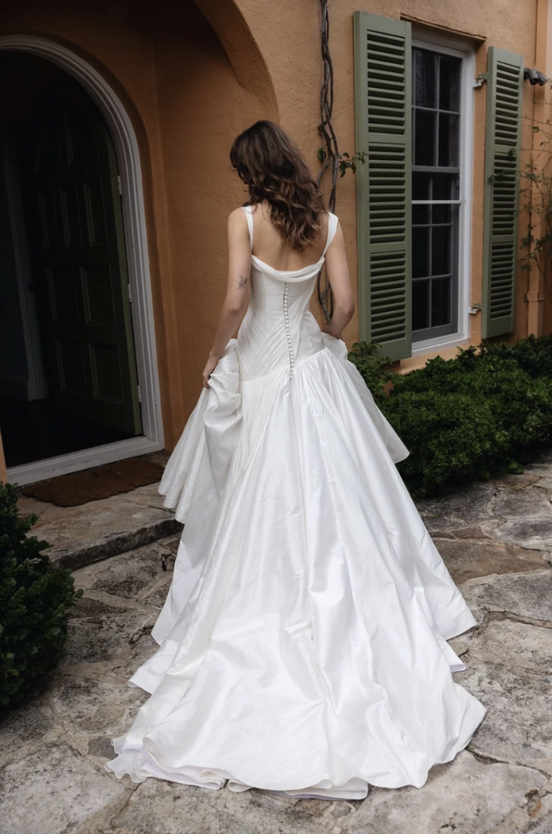 Back view of the J. Andreatta Nique wedding dress, showing a structured bodice, draped neckline, button detailing and full gathered skirt with a sweeping train.