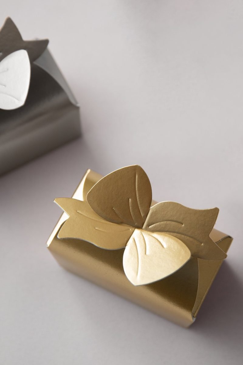 Gold wedding favor box with a metallic butterfly detail styled on a soft white linen surface.